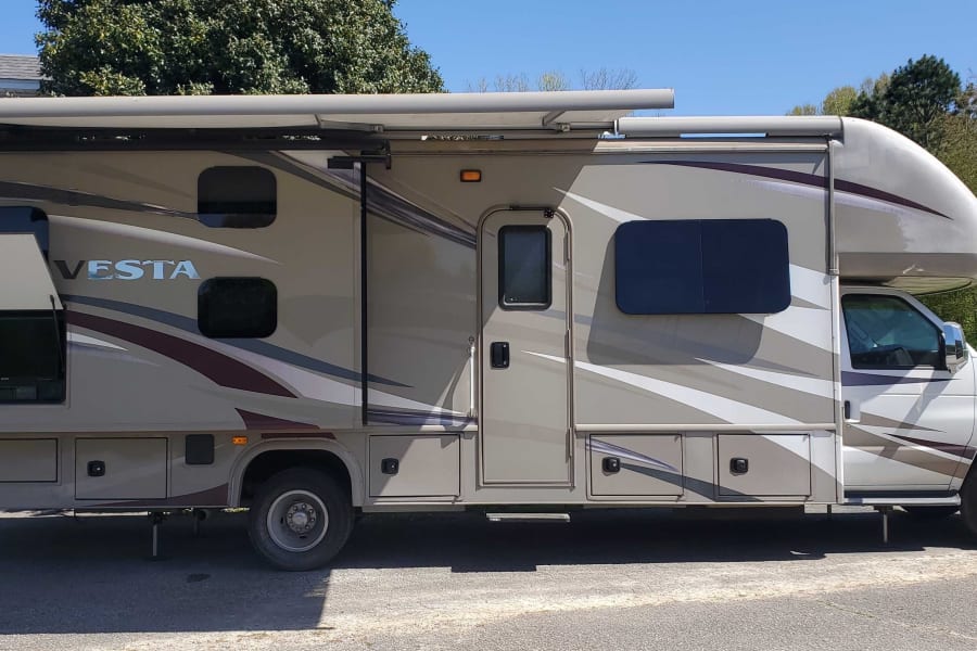 Side view of a spacious beige RV rental, featuring an open outdoor TV compartment and extended awning. Perfect for trips.
