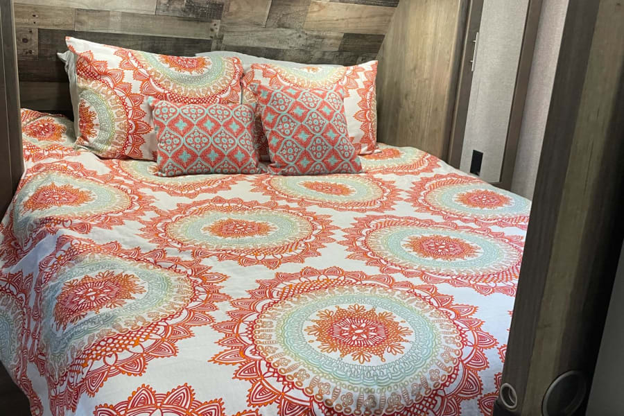 Cozy RV rental bedroom featuring a bed with vibrant mandala bedding, wooden headboard, and decorative shelf. Perfect for travelers.