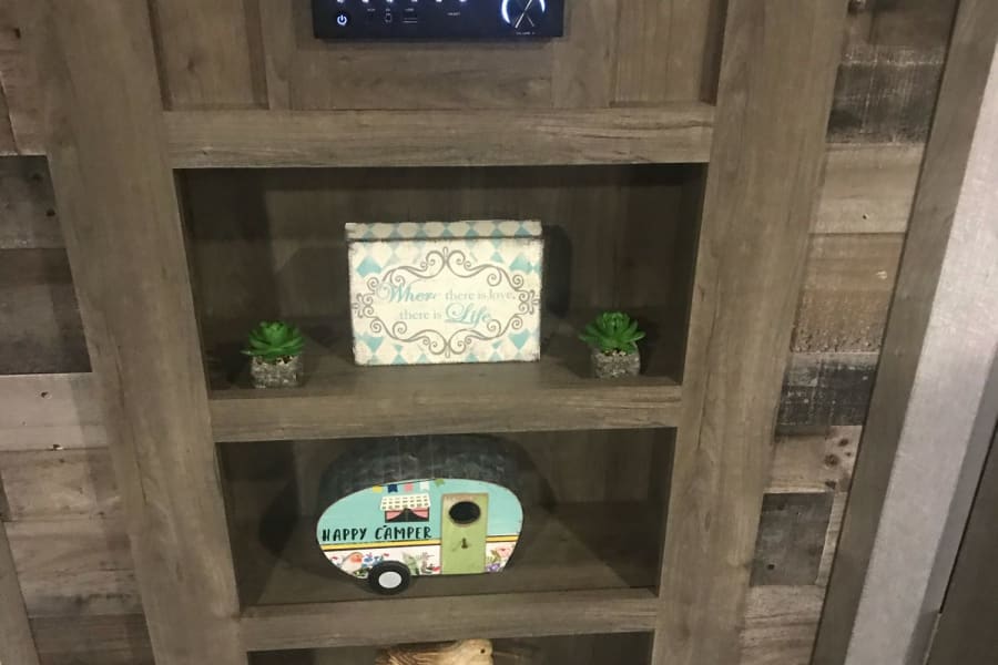 Inside an RV rental: built-in wooden shelves display a Furrion stereo, "Happy Camper" decor, and succulents.