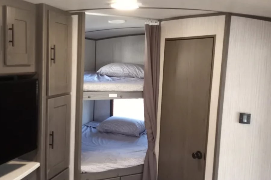 Cozy RV rental interior featuring modern bunk beds, storage cabinets, and a side door.