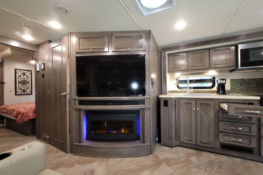 Spacious modern RV rental interior with kitchen, living area (TV, fireplace), and bedroom, perfect for a cozy trip.