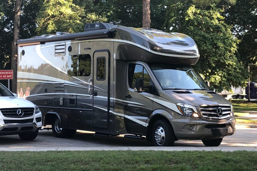 A polished, two-tone Mercedes-Benz motorhome, ideal for rv rental, parked roadside. Its large size and sleek design with chrome details are prominent.