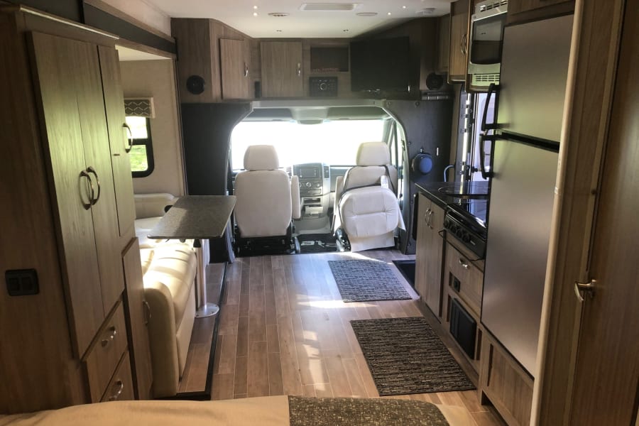 Inside a modern rv rental: kitchen with stove/fridge, comfortable living space, and driver's cockpit.