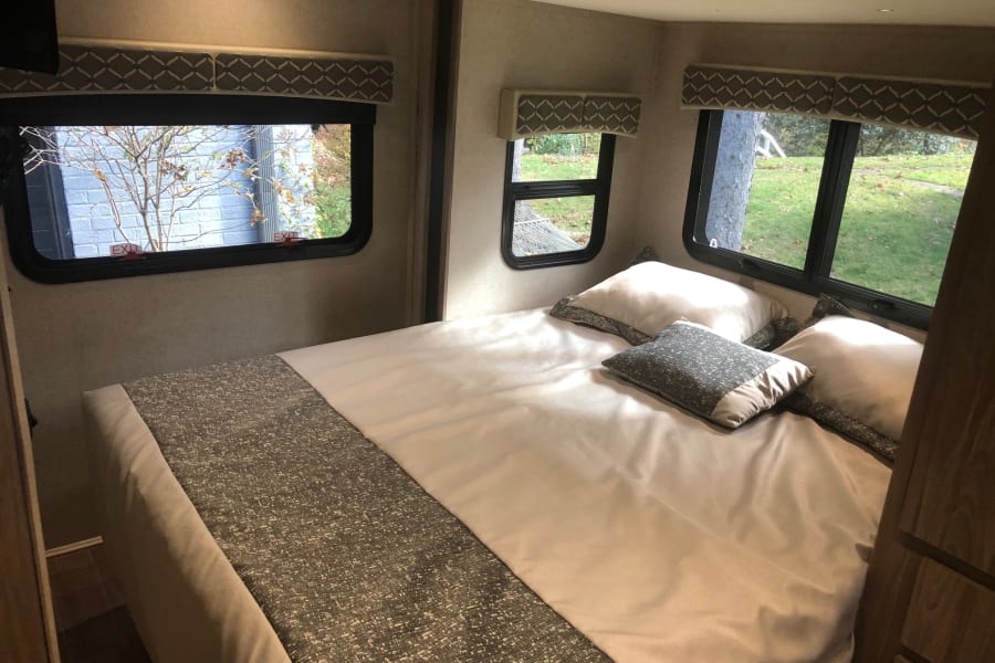 Bright RV rental bedroom: cozy bed, multiple windows with "EXIT" labels, and outdoor views. Great for travel.