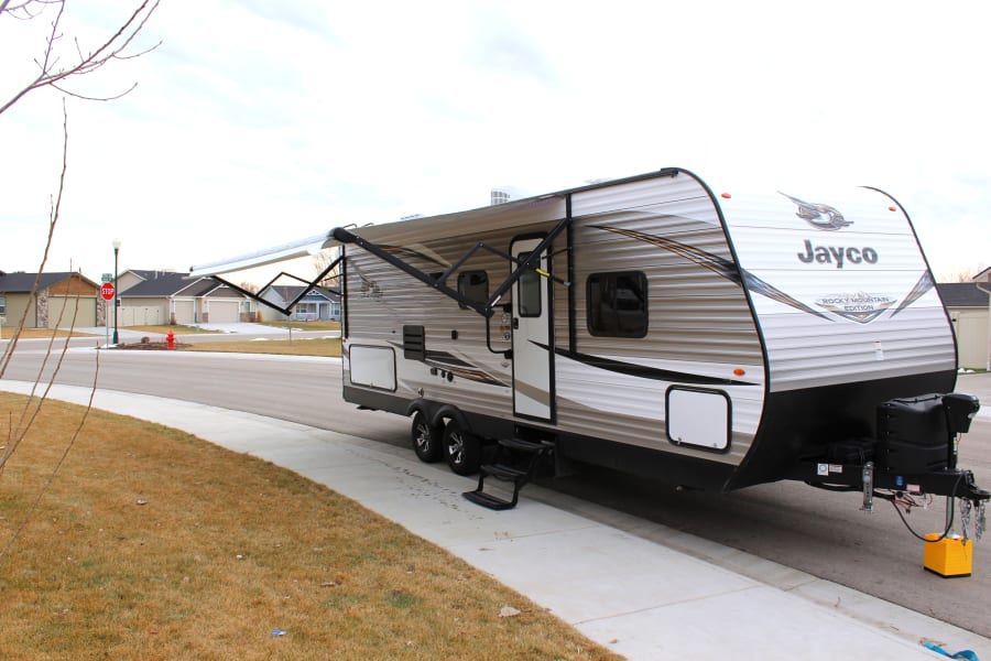 Jayco travel trailer RV rental with awning extended on a suburban street, ideal for your next trip.