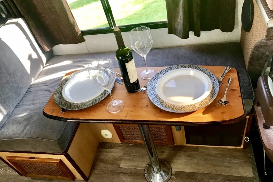 Cozy RV rental dining area: A wooden table set for two with plates, wine glasses, and a wine bottle.