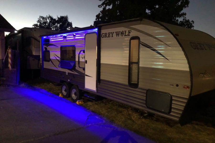 A Grey Wolf travel trailer, an ideal RV rental, glows with vibrant blue LED awning lights at night.