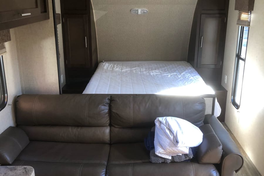 Interior of an RV rental: a spacious living area featuring a comfortable brown couch, leading to a queen-sized bed in the back.