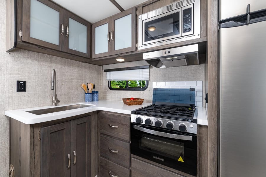 Modern and compact RV rental kitchen with essential appliances: microwave, stove/oven, fridge, sink, and ample cabinet space.