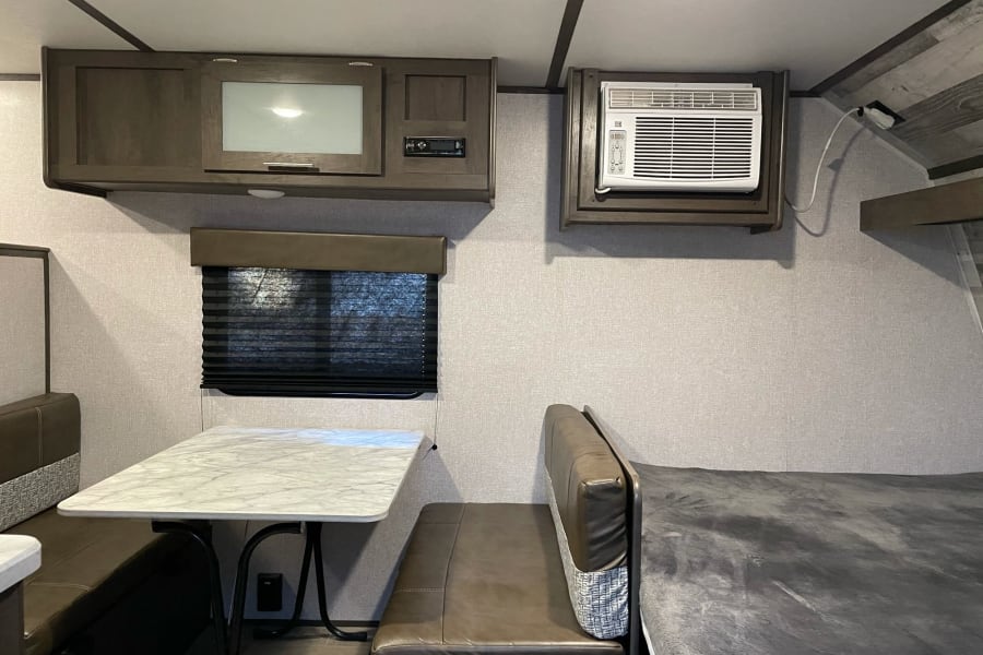 Spacious RV rental interior featuring a dinette, overhead cabinets, AC, entertainment system, and bunk bed for comfortable travel.