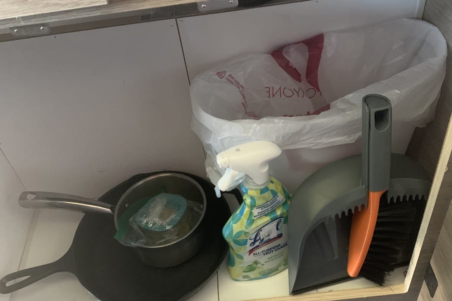 RV rental under-counter storage: Lys Lysol cleaner, dustpan/brush, skillet, and trash bag for compact living.