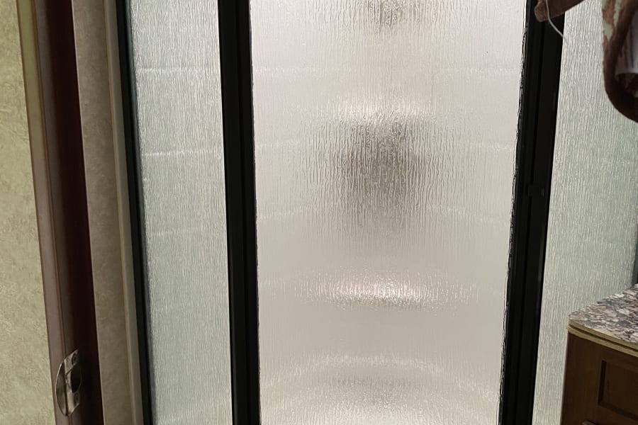 This RV rental shower enclosure features frosted glass panels and a black frame, providing privacy in a compact bathroom.