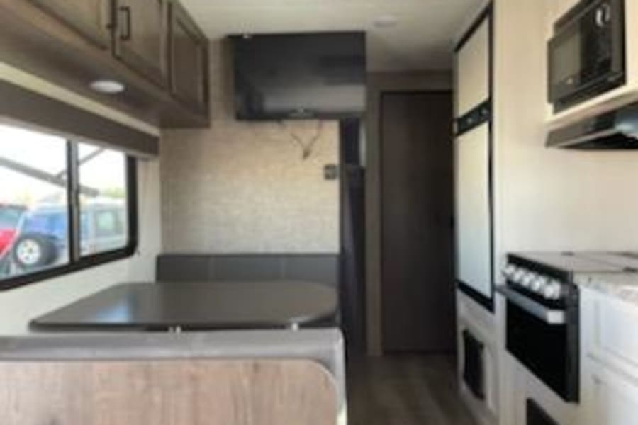 This RV rental features a well-equipped kitchen with stove, microwave, and fridge, alongside a comfy dining booth. Compact and ready for adventure!