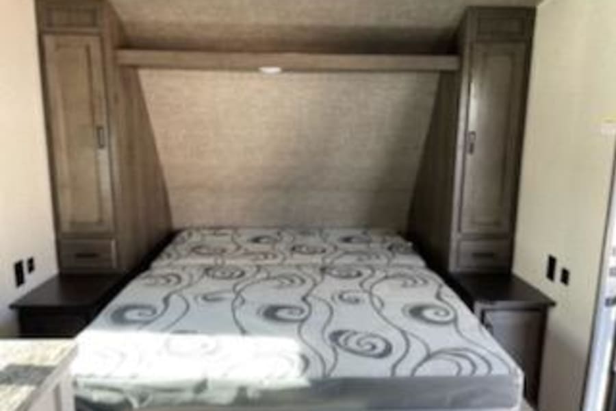 RV rental: Bright view of an RV bedroom showing a bed, integrated nightstands, and tall storage cabinets.