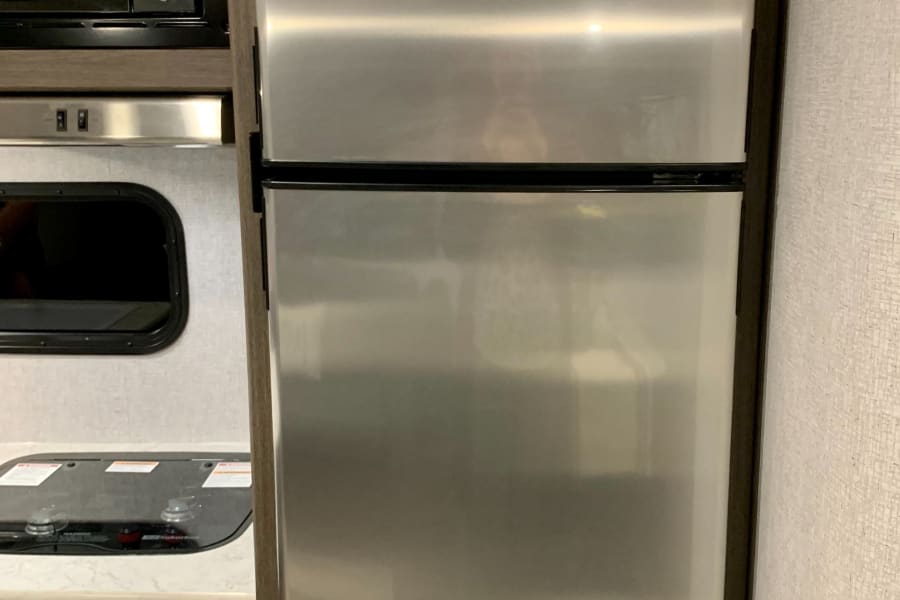 RV rental kitchen showing a stainless steel refrigerator, microwave, and cooktop. Built-in appliances for comfortable travel.