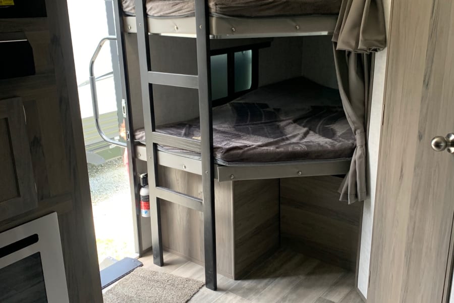 RV rental interior features modern bunk beds with ladder, wood-look flooring, and ample windows. Perfect for family adventures.