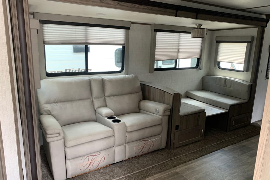 RV rental interior: cozy living space with Thomas Payne reclining sofa, cup holders, and dinette near windows.