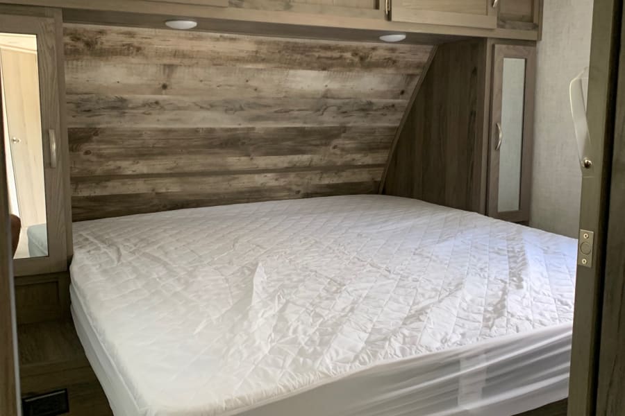 Inside a modern RV rental bedroom: white bed, wood-look walls & built-in storage. Compact comfort.