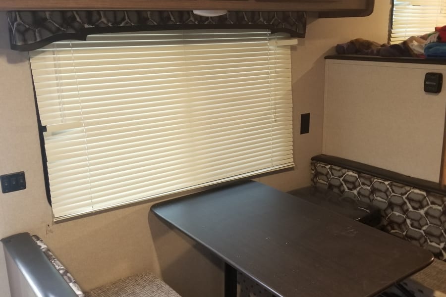 RV rental interior: dinette with dark table & patterned benches, overhead cabinets, stereo, and window blinds.