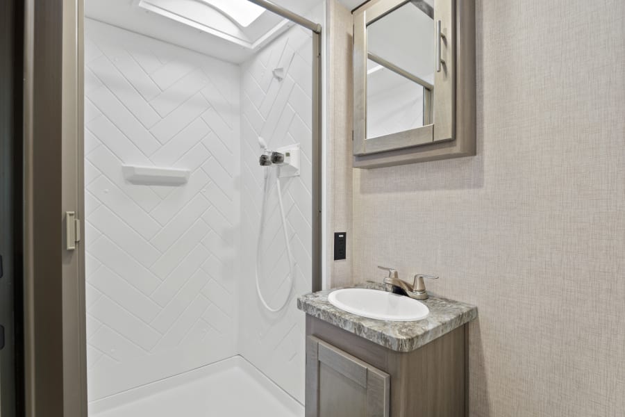 Modern RV rental bathroom with a stylish shower, skylight, vanity, sink, and mirrored cabinet.
