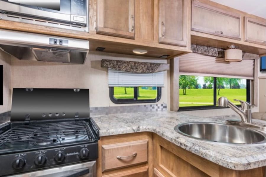 Spacious RV rental kitchen features microwave, stove, sink, wood cabinets & a scenic window view.