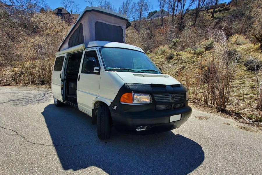 White pop-top VW camper van parked on a sunny road with open door. Ideal for your next rv rental adventure!