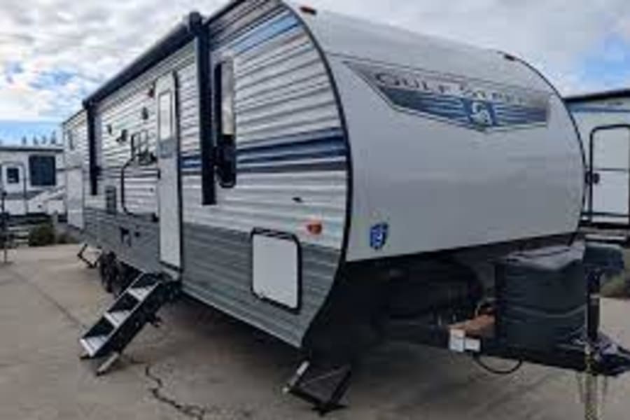 Ready for your RV rental? This grey/blue Gulf Stream travel trailer with steps down offers easy camping adventure.