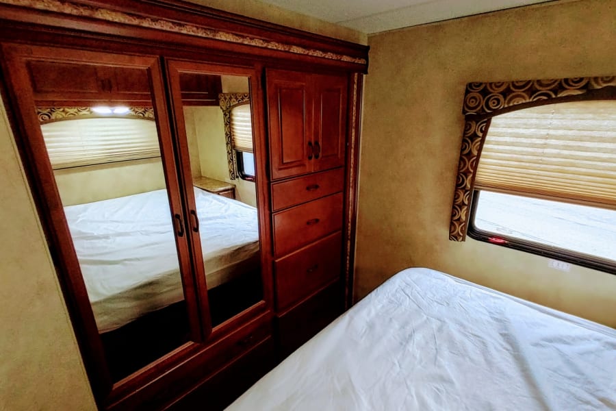 RV rental bedroom featuring a large mirrored closet reflecting the bed, a comfortable sleeping area, and a window.