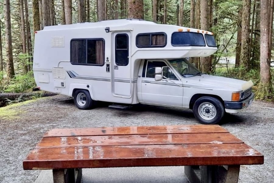 Classic RV rental at a serene forest campsite, with a rain-kissed picnic table in the foreground.