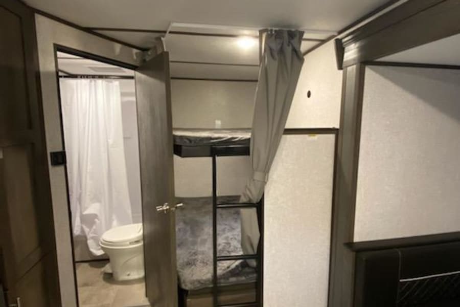 This RV rental interior features bunk beds, a compact bathroom with a toilet, and dinette seating, ideal for travel.