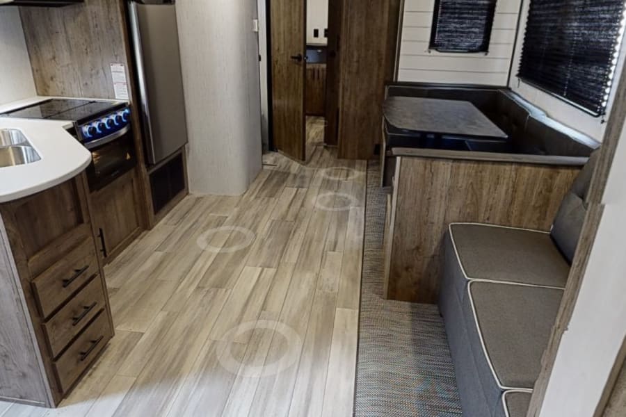 Bright rv rental interior: kitchen with stove & fridge, dining booth, and cozy seating. Perfect for road trips.