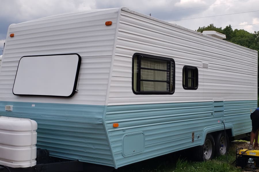 Two-tone white and blue rv rental travel trailer, featuring side windows, dual axles, and a front propane tank.