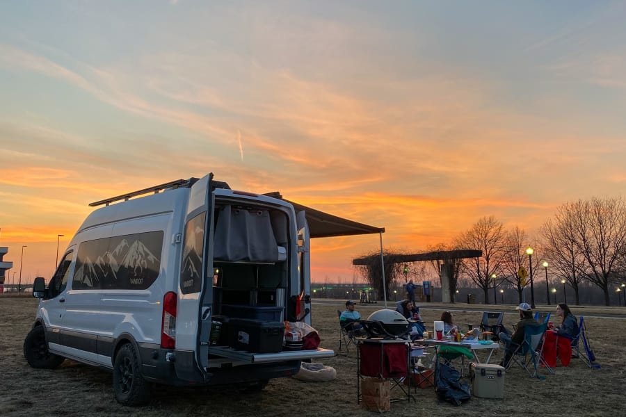 Vibrant sunset view: Friends enjoy outdoor cooking by a Vandoit RV rental camper van.