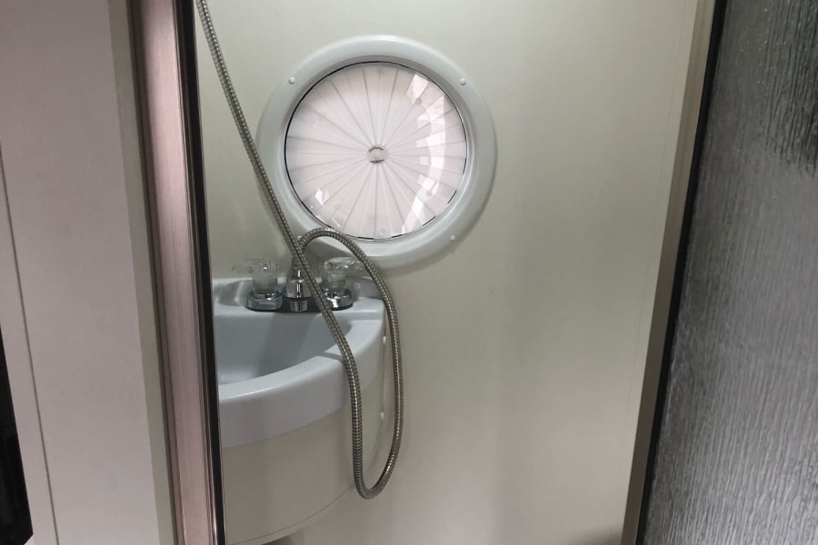 RV rental wet bath: compact shower, sink, and toilet with a unique round window.