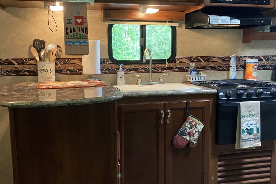 RV rental kitchen: brown cabinets, microwave, stove, sink, and TV. Cozy & functional for your next adventure.