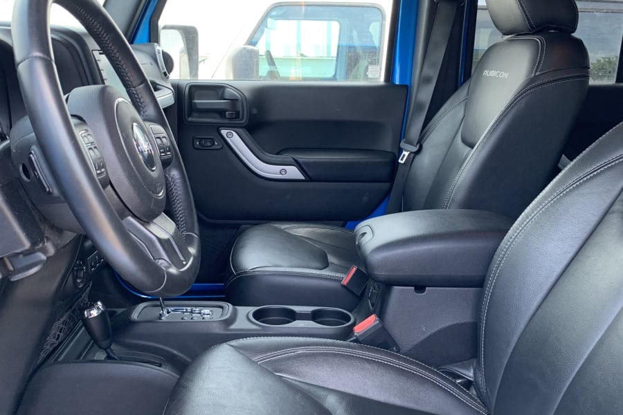 Blue Jeep Wrangler Rubicon interior: black leather seats, detailed steering wheel. Ready for your RV rental adventure!