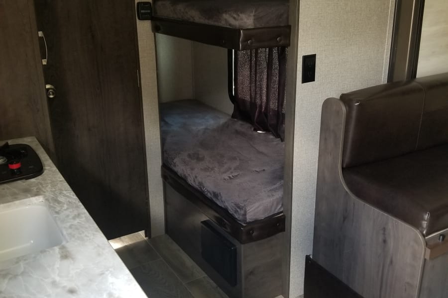 This RV rental interior features a kitchen counter, a dark wood door, bunk beds, and a dinette area.