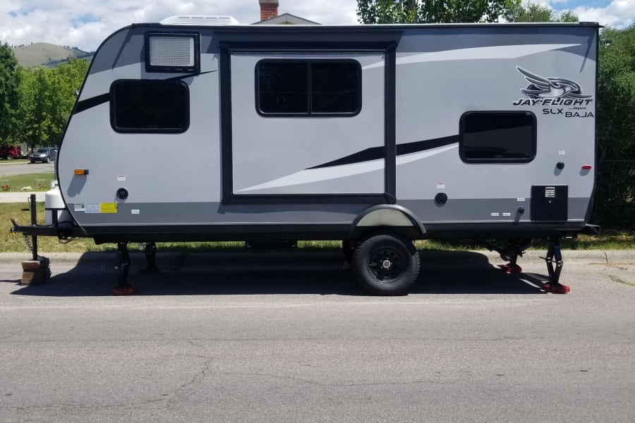 This grey Jayco Jay Flight SLX Baja travel trailer is parked & ready for your next rv rental adventure under blue skies.