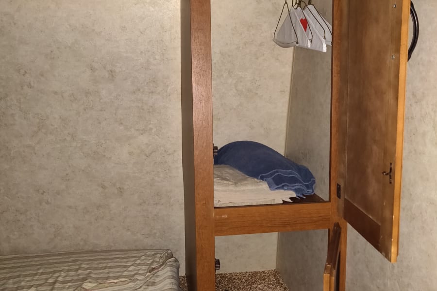 Inside an RV rental: a cozy bed, open closet with hanging space & folded towels, plus lower storage.