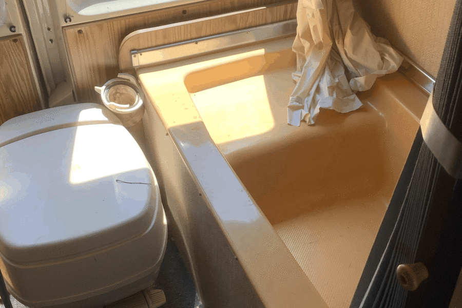 Compact RV rental bathroom featuring a white toilet, integrated shower/tub, and a window showing an external tire.