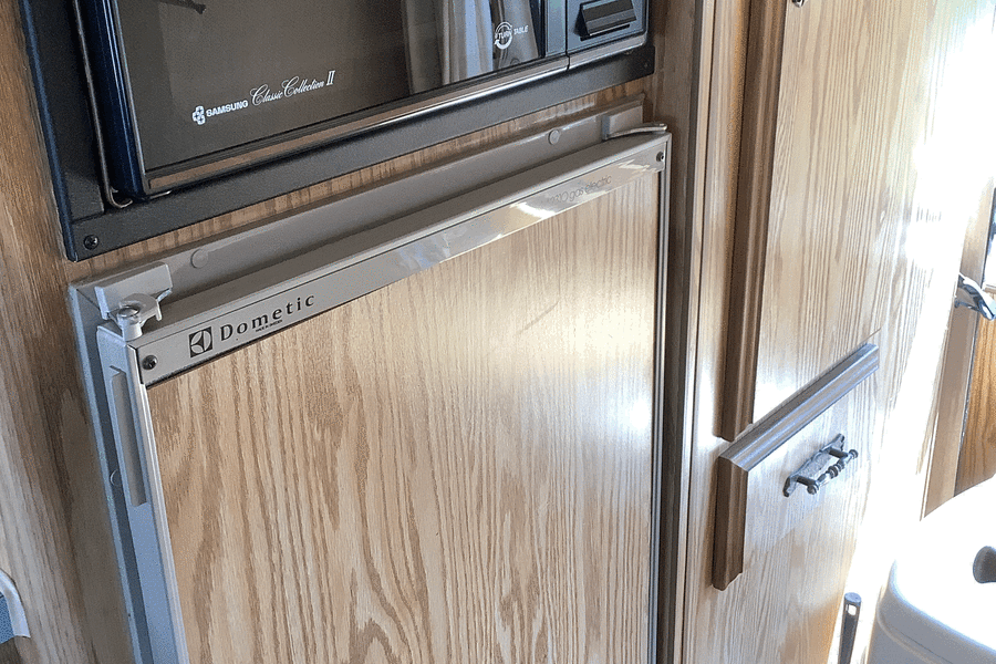 RV rental: Samsung microwave, Dometic gas-electric fridge, and toilet brush in compact living space.
