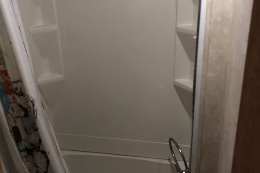 Compact RV rental bathroom features a white shower/tub combo with built-in shelves and a colorful shower curtain.
