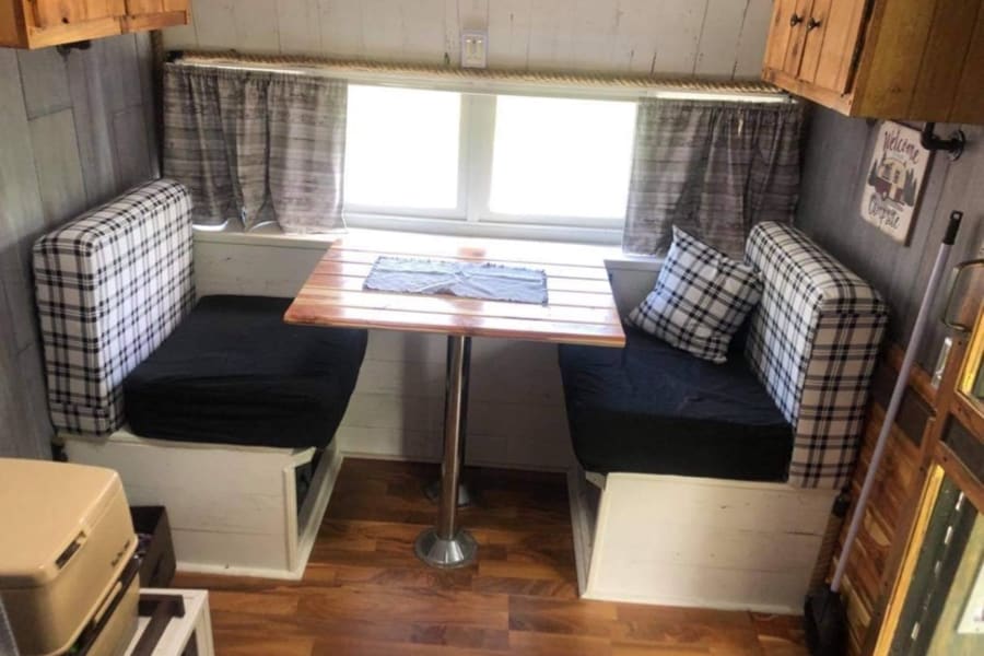 Cozy RV rental dinette with plaid benches, wood table, and window views. Perfect camper interior.