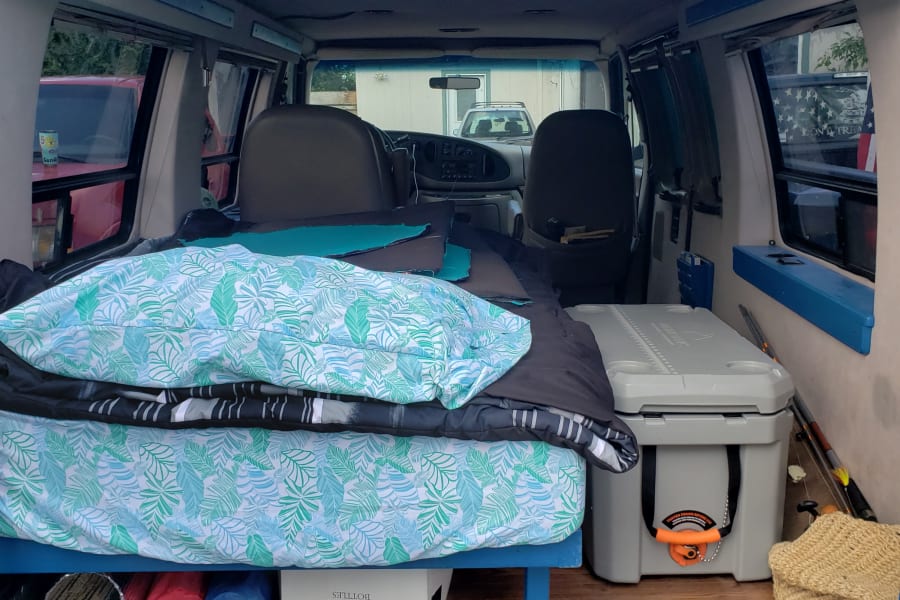 Cozy van interior, ideal for rv rental, featuring a comfortable bed, large cooler, and under-bed storage.