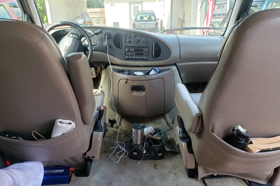Inside an RV rental Ford van: dashboard, front seats, and floor with a power inverter & supplies for travel.