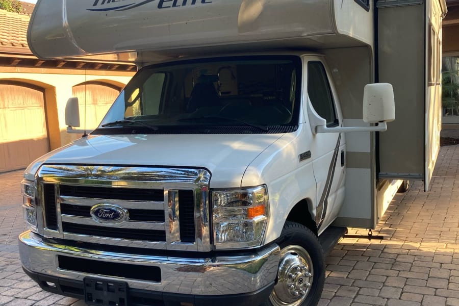 White Ford E-450 Freedom Elite RV rental parked on pavers, with slide-out extended, under a clear sky.