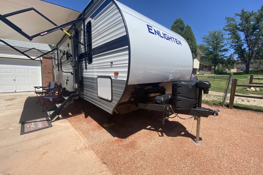 Spacious 'Enlighten' travel trailer RV rental parked with awning extended, two chairs set up. Ready for your adventure!
