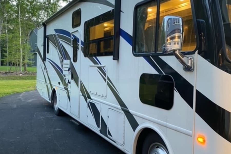 A modern white RV motorhome with black/blue stripes, parked. Interior lights glow, perfect for your next rv rental journey.