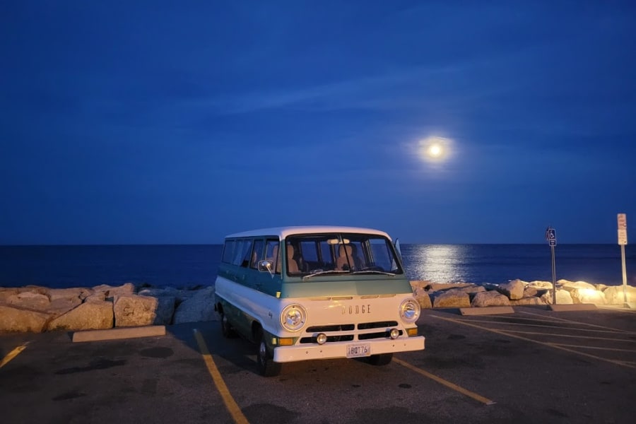 Vintage Dodge van, parked by the ocean under moonlight. Your next RV rental adventure awaits!