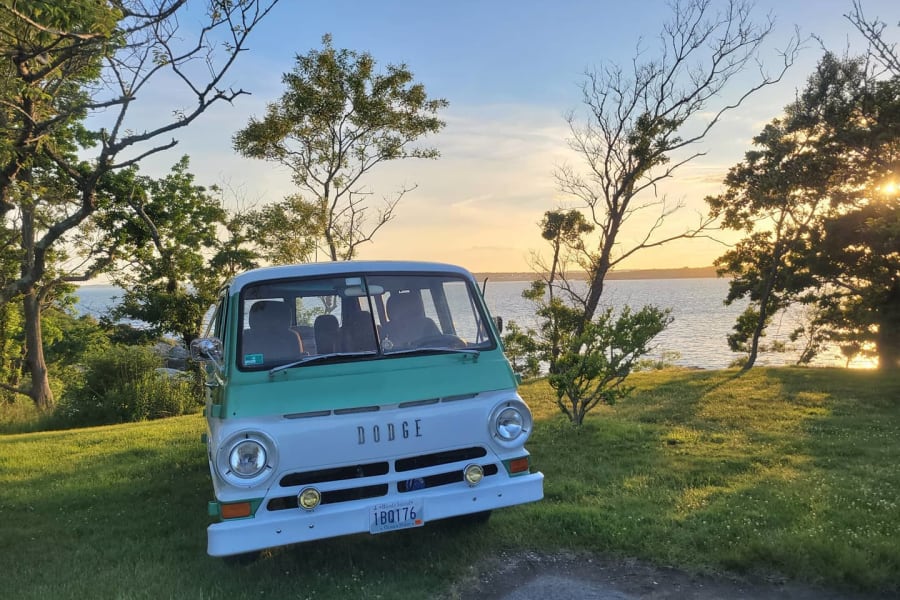 Two-tone vintage Dodge van by the ocean at sunset. Imagine this classic RV rental adventure!